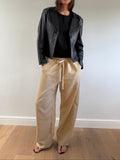 Person wearing a black jacket, black shirt, and beige pants on a plain background