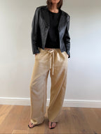 Person wearing a black jacket, black shirt, and beige pants on a plain background