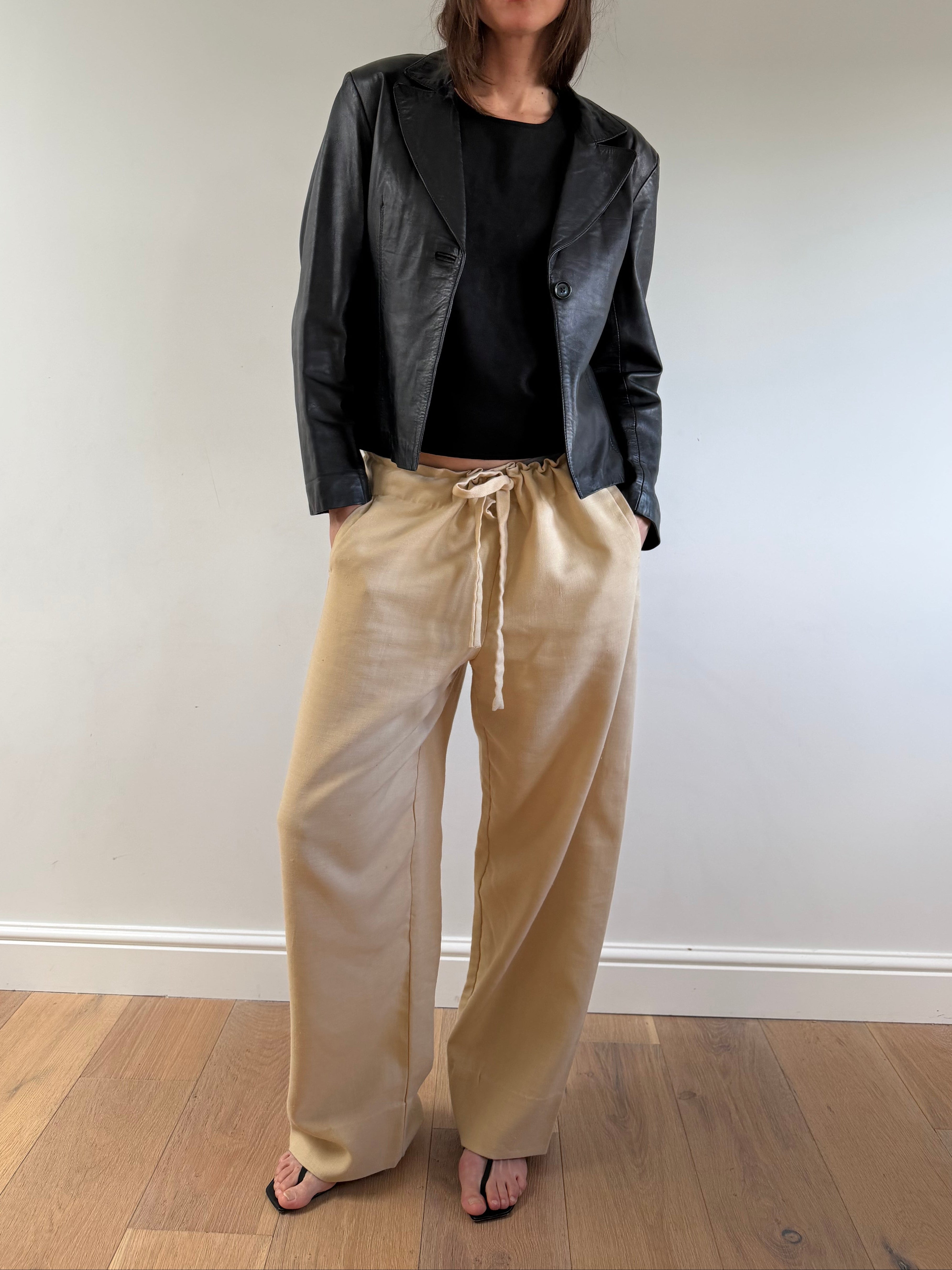 Person wearing a black jacket, black shirt, and beige pants on a plain background