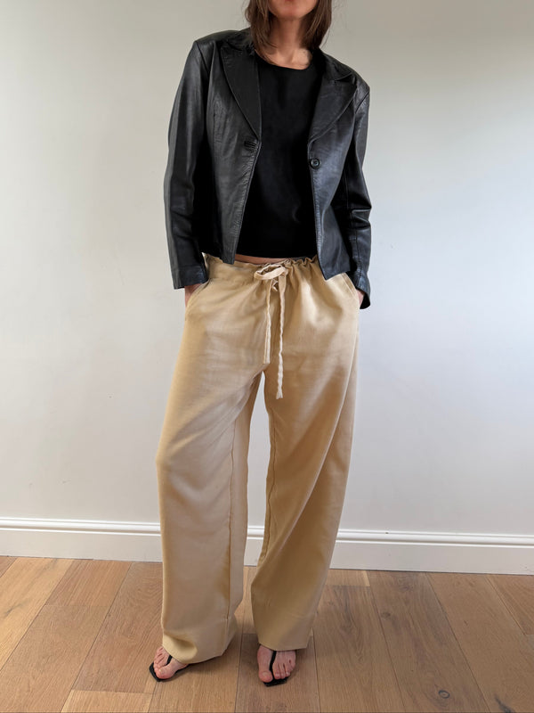 Person wearing a black jacket, black shirt, and beige pants on a plain background